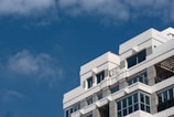 A modern university campus building with clean white walls and blue accents under a clear sky.