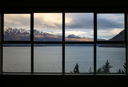 calm body of water near brown mountain under white and gray sky in Queenstown New Zealand