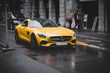 yellow Mercedes-Benz coupe on asphalt road near concrete building