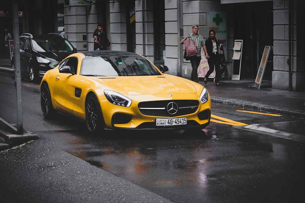 Mercedes-Benz coupé amarillo en una carretera asfaltada cerca de un edificio de hormigón