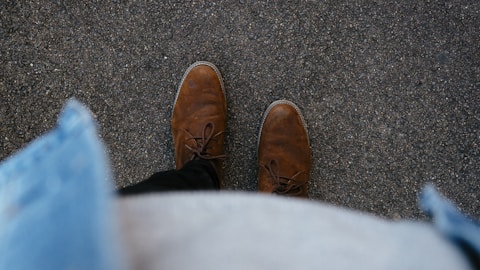 person wearing pair of brown leather boots standing on asphalt surface