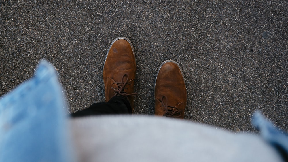 Person, die ein Paar braune Lederstiefel trägt, die auf einer Asphaltoberfläche steht