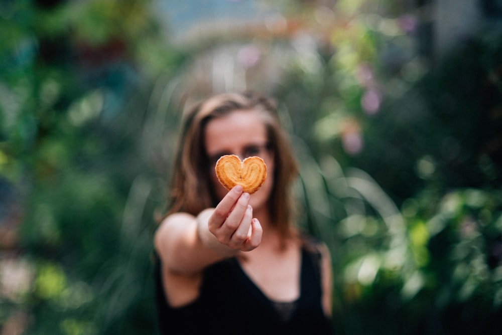 mujer en top negro sosteniendo galleta en forma de corazón