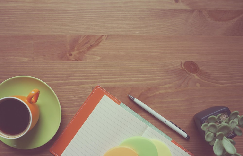 white pen beside notebook and coffee cup