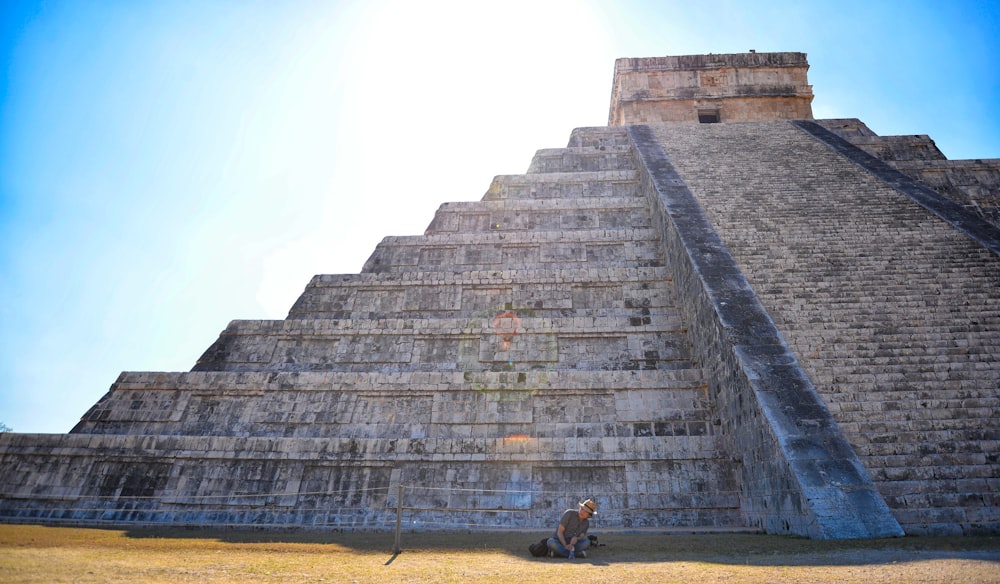 person sitting on grass field in front on gray concrete pyramid