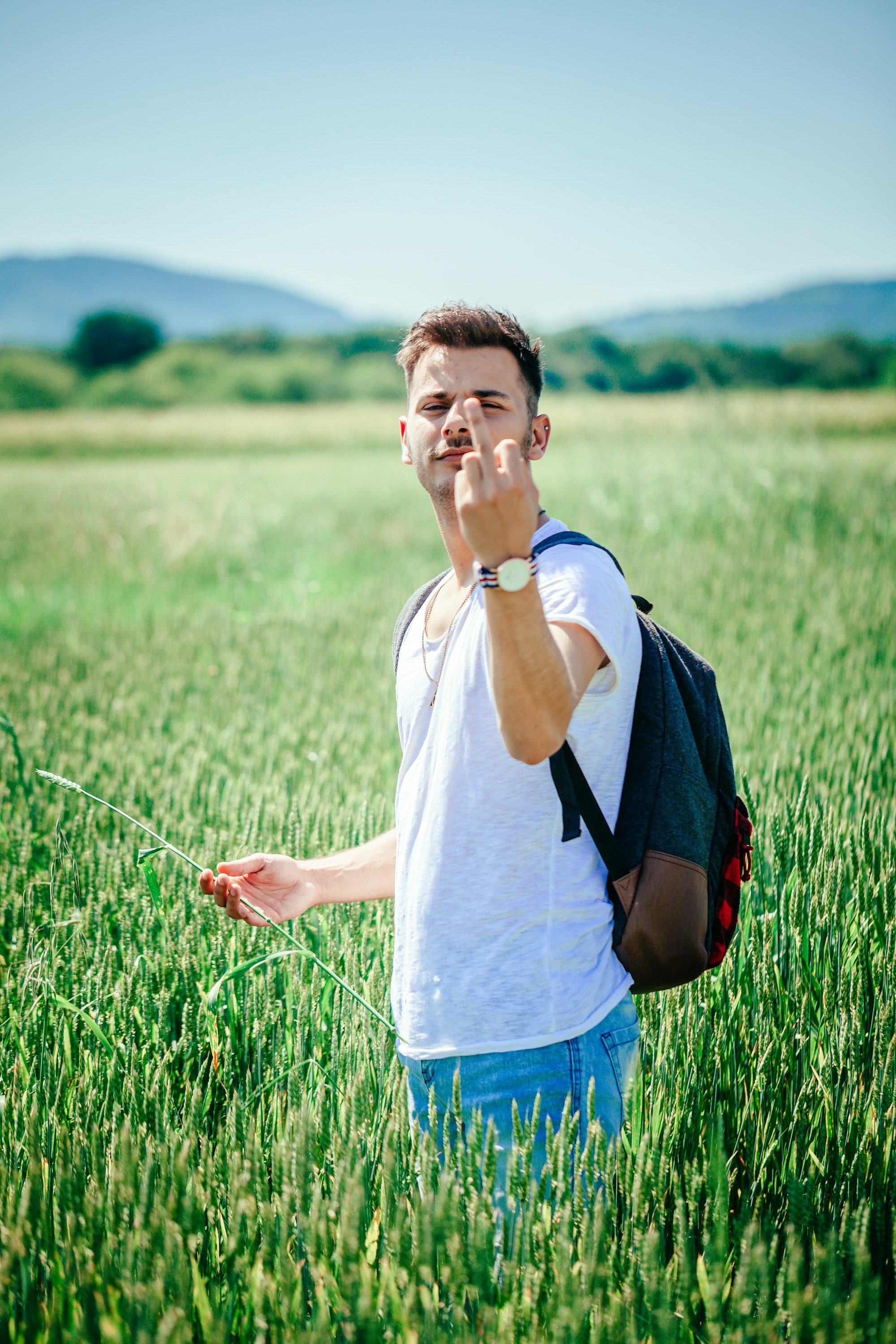 Young hippster guy in wheat field showing middle finger