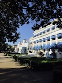 Buildings with white exteriors and blue awnings are aligned along a tidy, green lawn. A sidewalk runs parallel to the buildings, with trees providing shade. The sky is clear and blue. The main building is marked with 'Buckstaff Baths.'
