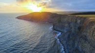 Coastal cliff view with calm waves and a golden sunset.