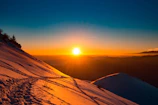 Sunset casting golden light over a snowy mountain ridge with ski tracks winding down.