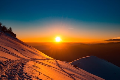 Sunset casting warm light over a snowy mountain ridge with ski tracks.