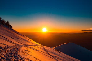 Sunset casting golden light over a snowy mountain ridge with ski tracks winding down.