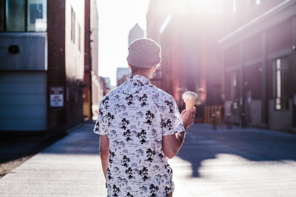 Stehende Person in weißem, schwarzem und grauem T-Shirt mit Kragen, Eis in der Hand und mit Blick nach hinten