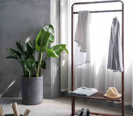 gray dress shirt hang on brown wooden rack in front of window with white curtain