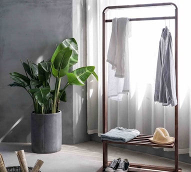 gray dress shirt hang on brown wooden rack in front of window with white curtain