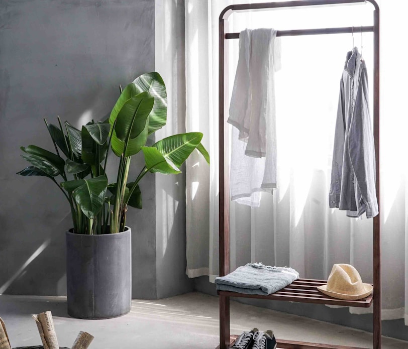 gray dress shirt hang on brown wooden rack in front of window with white curtain