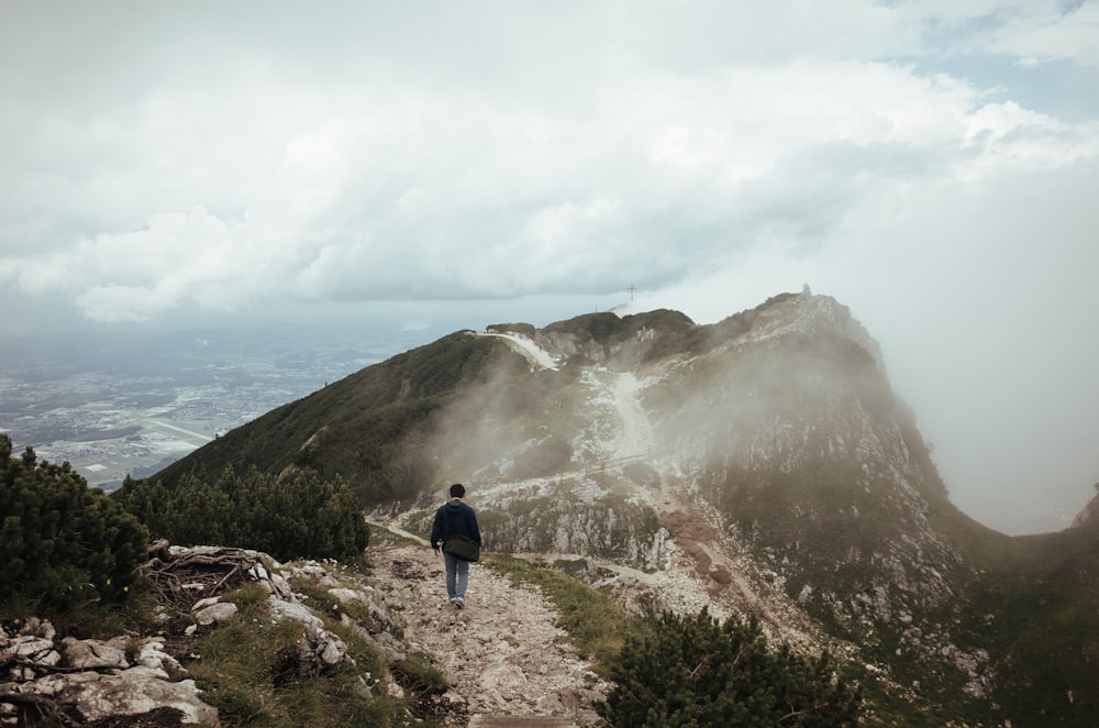 person wearing black top walking towards mountain covered with fog during daytime