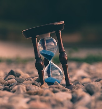 selective focus photo of brown and blue hourglass on stones