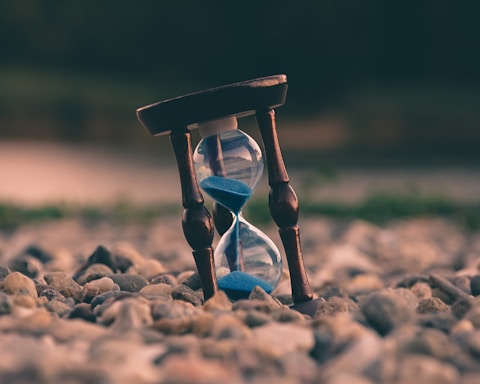 selective focus photo of brown and blue hourglass on stones