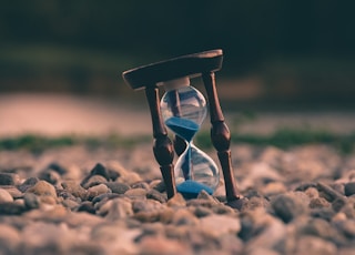 selective focus photo of brown and blue hourglass on stones