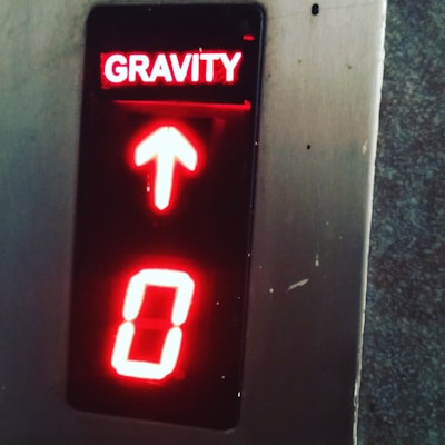 An illuminated panel with the word 'GRAVITY' in red letters above an upward pointing arrow and the number '0' below, all surrounded by a metallic frame.