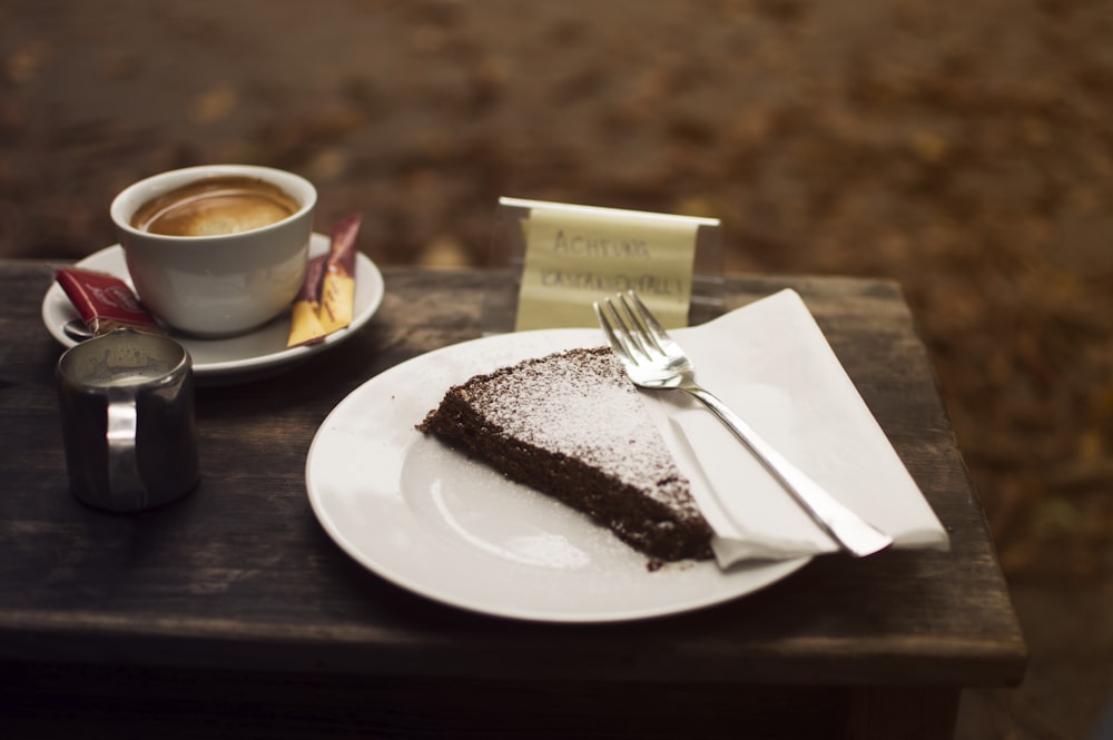 prato de bolo fatiado com garfo de prata ao lado de xícara de café em tábua de servir de madeira marrom