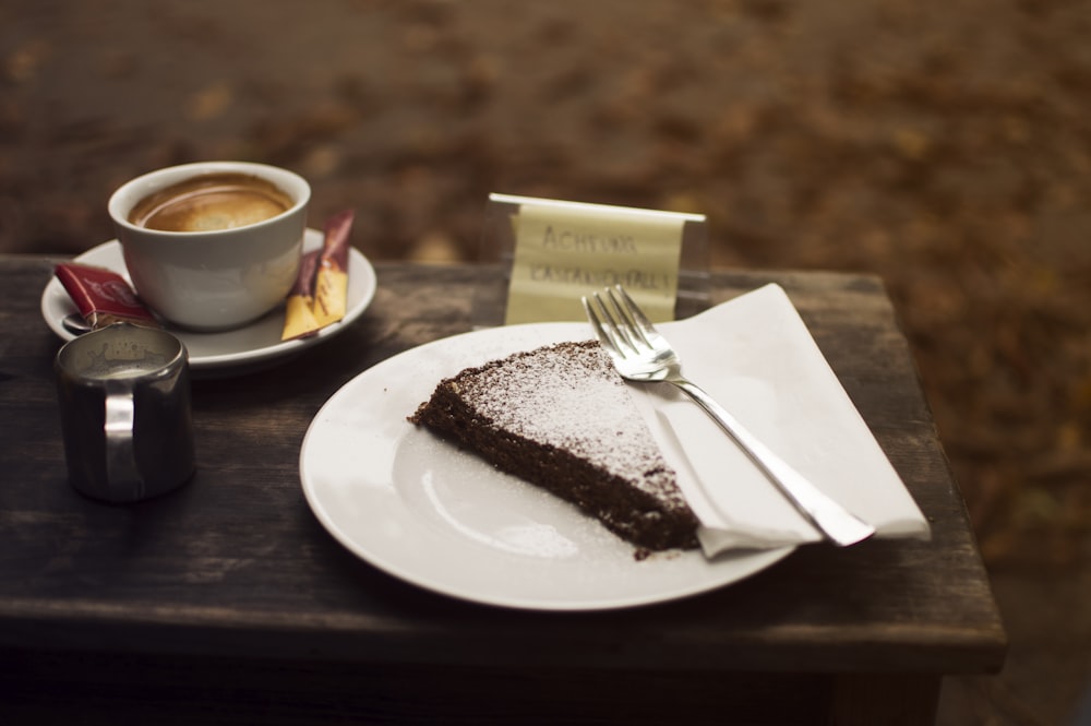 plate of sliced cake with silver fork beside cup of coffe on brown wooden serving board