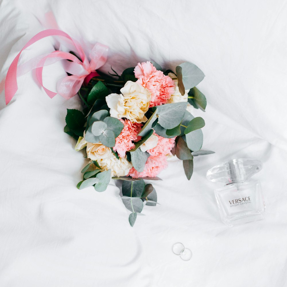 bouquet de roses et de chrysanthèmes jaunes et roses placés à côté d’un vaporisateur Versace sur textile blanc