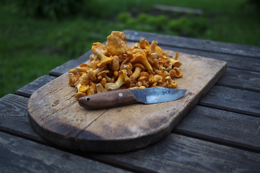 brown wooden chopping board with brown mushrooms on top beside knife