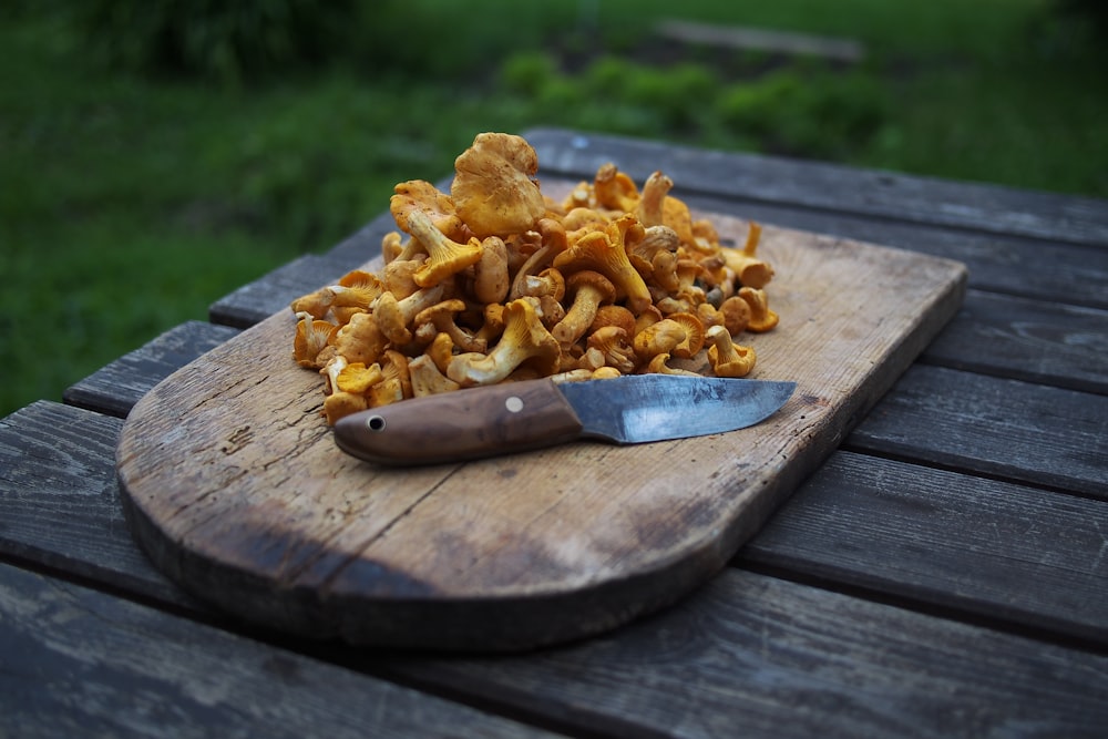 planche à découper en bois brun avec des champignons bruns sur le dessus à côté du couteau