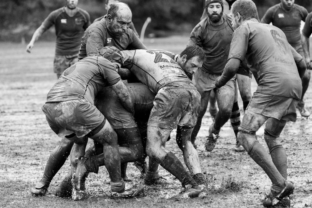 grayscale photography of group of people playing rugby on muddy field