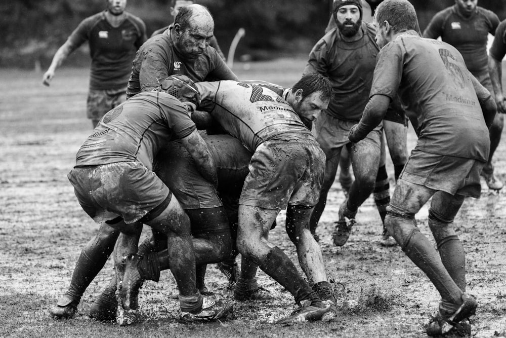 grayscale photography of group of people playing rugby on muddy field