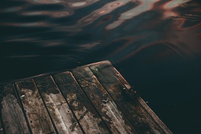A weathered wooden dock stretching into calm seafoam-green waters under soft morning light