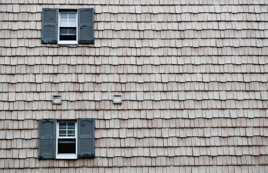 A shingled wall with two shuttered windows