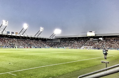 A dynamic shot of a cameraman filming a fast-paced soccer match under stadium lights.