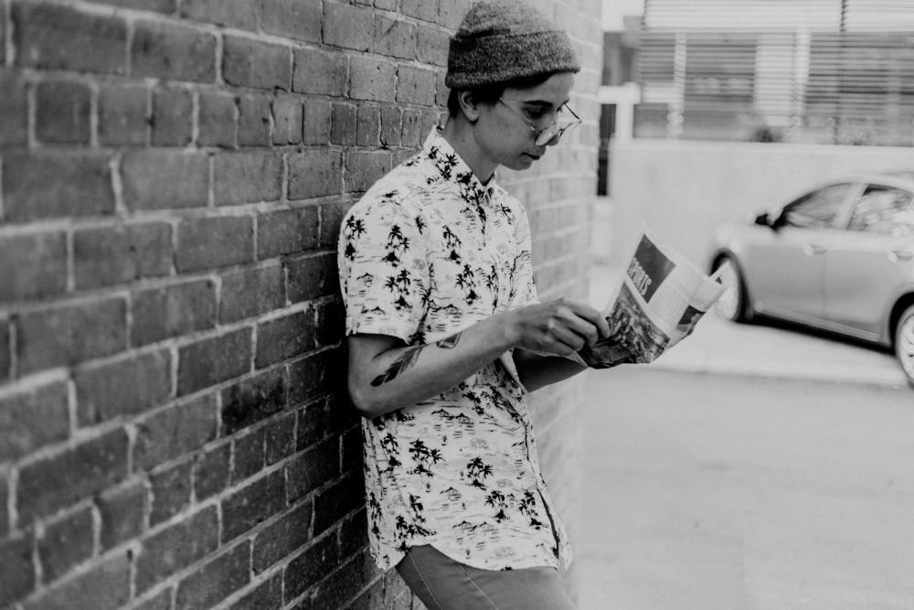 grayscale photo of man leaning on wall