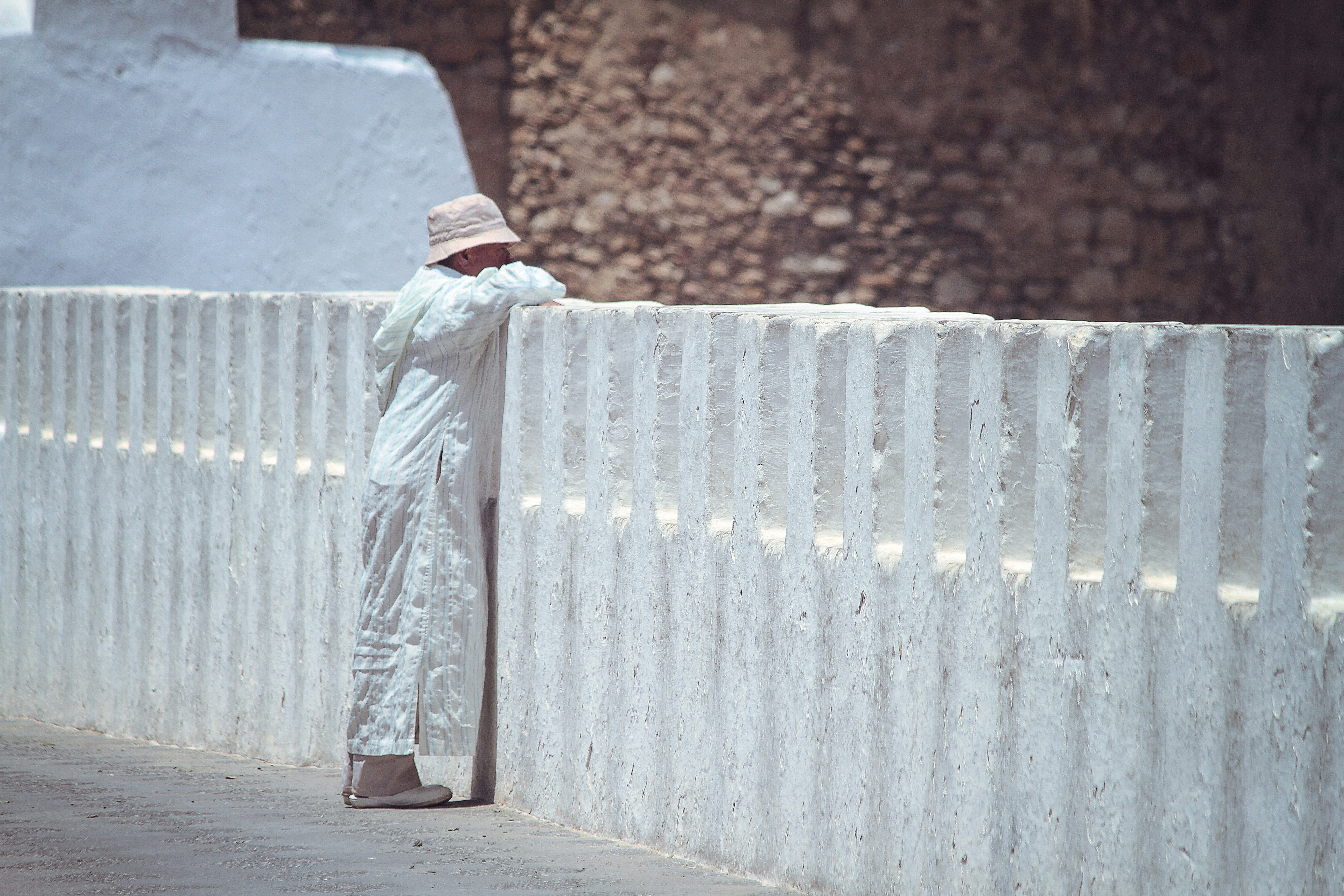 Persona con camisa blanca de manga larga y jeans de mezclilla azul de pie sobre piso de concreto marrón durante