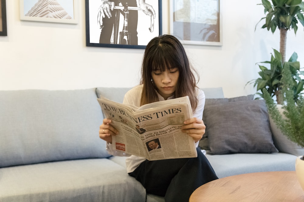 a woman sitting on a couch reading a newspaper