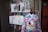 A mannequin is dressed in a colorful kimono with a floral and crane pattern. Several photo albums are displayed on a shelf above, showcasing images of people in similar attire. A large poster behind the mannequin features a person in traditional dress.