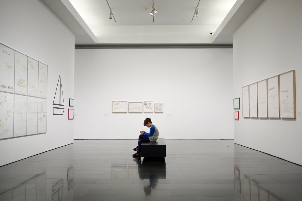 Boy sitting alone inside large gallery room with white walls viewing exhibition in Barcelona