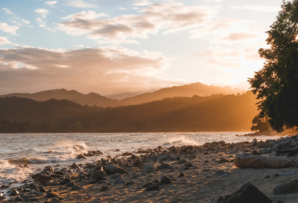 body of water near high mountains under white and blue sky at golden hour