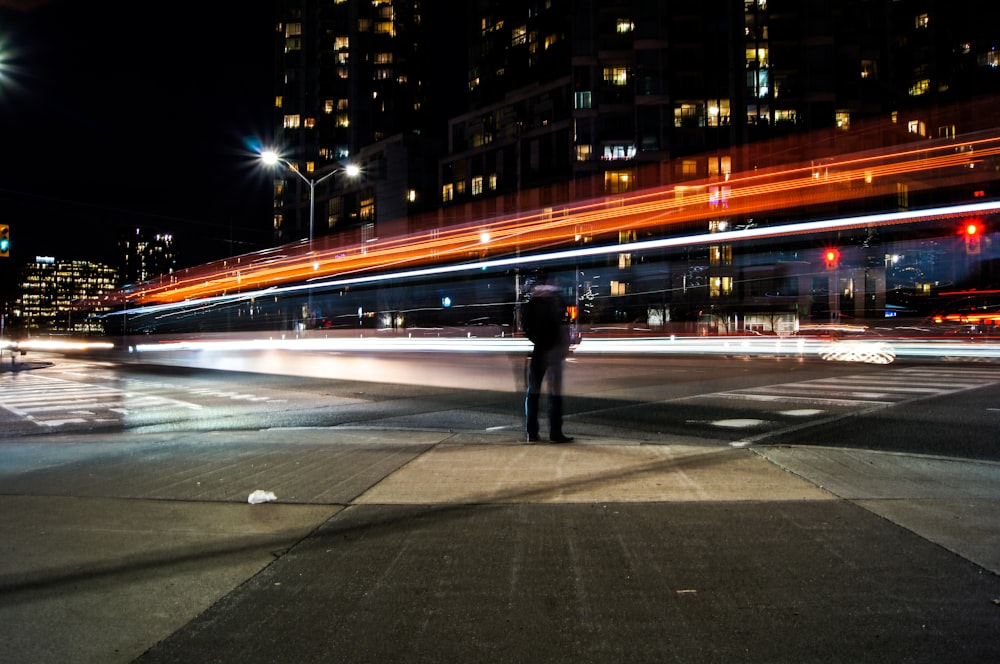 Fotografia time-lapse dell'uomo in piedi accanto alla strada e al ponte durante il giorno