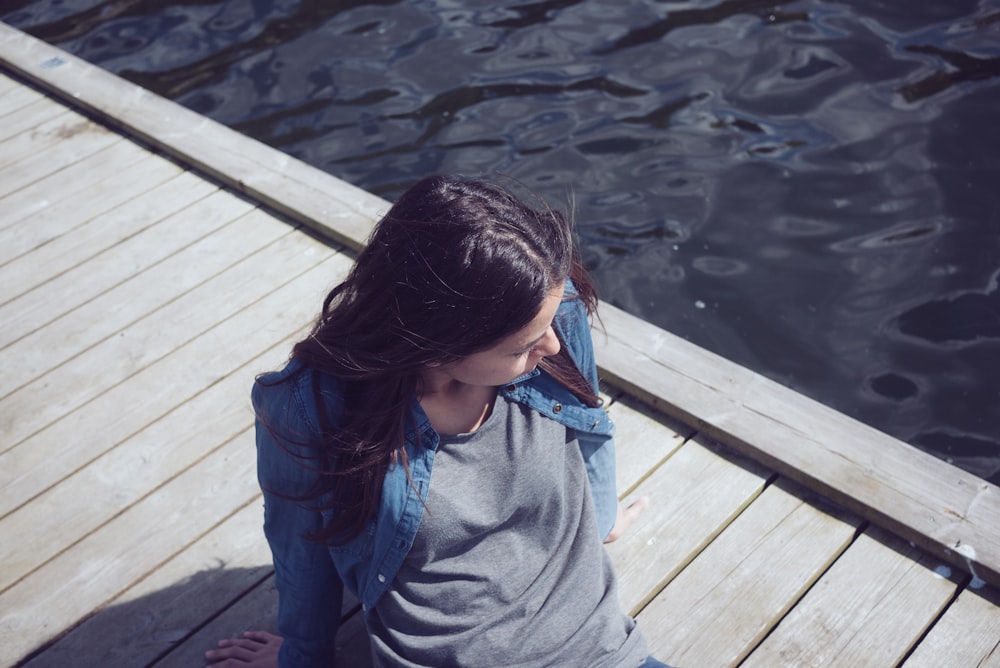 woman in grey top seating on dock during daytime
