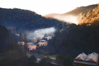 A quiet village nestled between rolling hills, with smoke gently rising from chimneys at dusk.