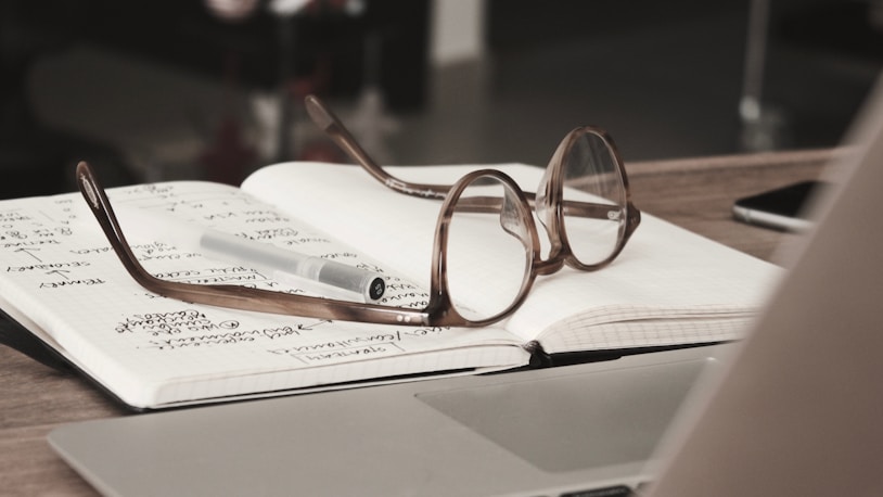 Glasses on an open notebook with notes, beside a laptop and smartphone, illustrating academic 