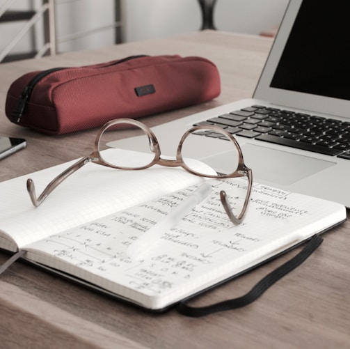 eyeglasses on book beside laptop