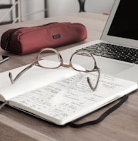 eyeglasses on book beside laptop