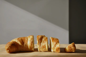 Close-up of a freshly baked golden croissant resting on a rustic wooden board with soft morning light.