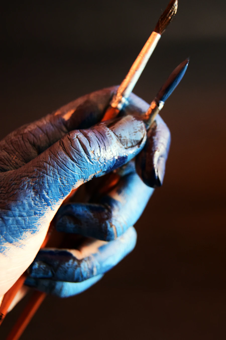 Paint-stained hands holding a paintbrush at the end of a long day of interior painting work, the mark of a working painter