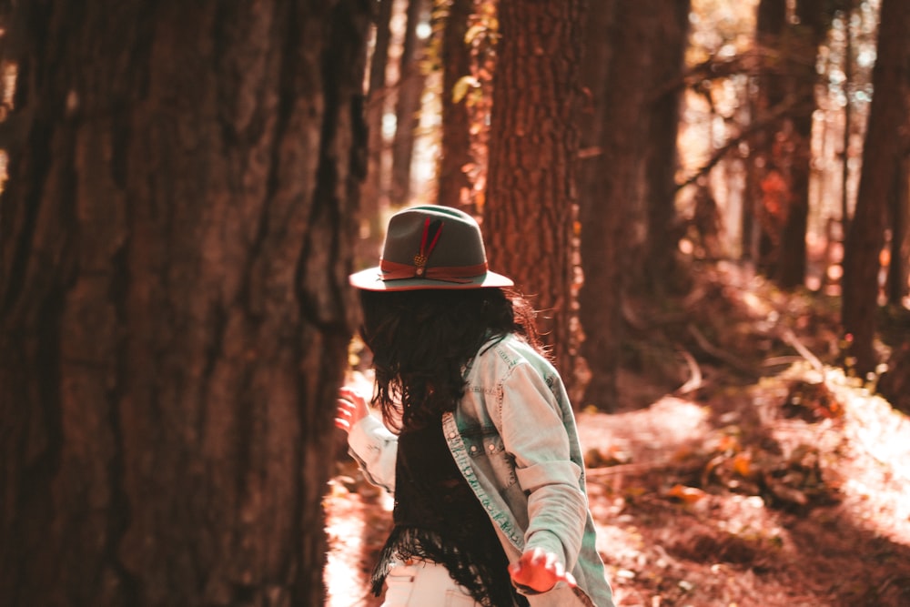 person wearing button-up long-sleeved shirt looking on tree inside forest