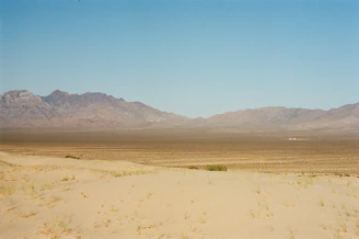 A panoramic view of the Tibesti mountains with desert dunes in the foreground under a clear blue sky.